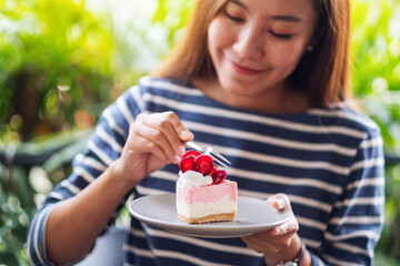 Closeup image of a beautiful young asian woman holding and eating a piece of strawberry cheese cake