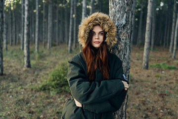 woman in warm jacket leaning on a tree on the background of the forest walk trip