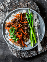 Healthy lunch - spicy stir fry beef, rice, asparagus on dark background, top view
