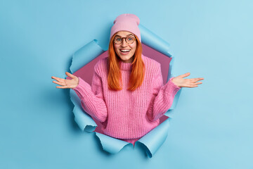 Beautiful cheerful redhead young woman shrugs shoulders feels confused as received unexpected offer...
