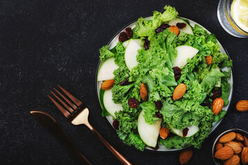 Vegan Kale salad with dried cranberry, apples and almonds. Healthy food, top view, black kitchen table