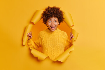 Happy amazed dark skinned woman looks with glad surprised expression, reacts on crazy news, smiles...