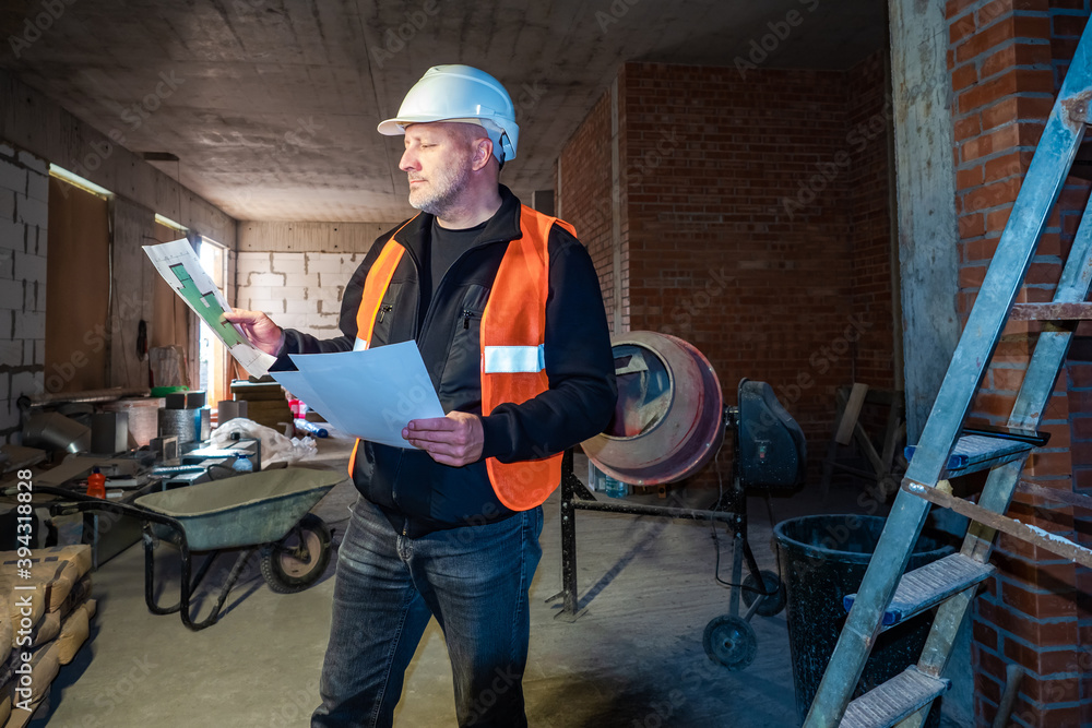 Poster a man in a white helmet studies construction drawings. engineer inside the building under constructi