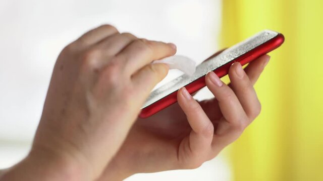 Close-up of woman hand using wet wipe and sanitizer to clean cell phone screen. People cleaning and disinfecting mobile telephone monitor to kill virus and germs. Female hands holding smartphone