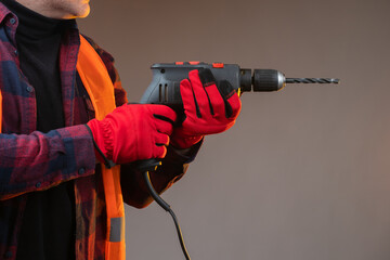 A man with a drill in his hands. Close-up of the perforator. A man in work gloves is holding a...