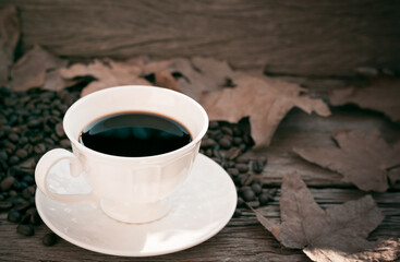 black coffee in white mug with maple leaf on wooden table in vintage style