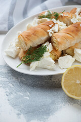 Closeup of greek baked mini filo rolls filled with feta cheese, vertical shot on a white concrete surface