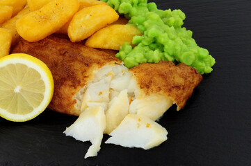 Battered cod fish fillet with chunky chips and mushy peas on a slate stone background