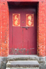 A Chinese styled old red wooden door with couplet and bolt on it. The Chinese Festival couplets meaning "prosperous state" and "people at peace".