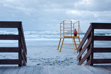 lifeguard chair on a sea side during stormy weather with big waves. View from a wooden promenade.