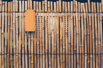 Fence made of bamboos with a blank wooden sign on it. Toned image.