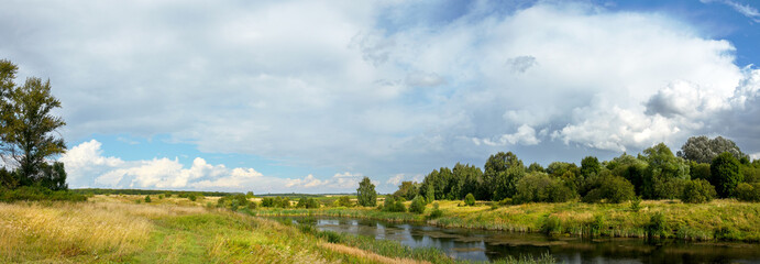 Panoramic summer rural landscape with calm lake and green hills in sunny day.