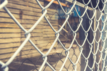 Closeup of metal net with a glass wall and a wooden house behind it. Toned image.