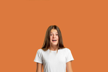 Scared child. Problem anxiety. Panic attack. Shocking news. Portrait of overwhelmed confused teen girl with open mouth in white t-shirt looking at camera isolated on red orange empty space background.