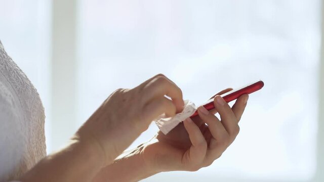 Close-up of woman hand using wet wipe and sanitizer to clean cell phone screen. People cleaning and disinfecting mobile telephone monitor to kill virus and germs. Female hands holding smartphone