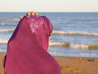 young girl with hand on veil on head by the sea at sunset