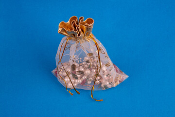Pearl necklace inside a gold transparent gift bag on a blue background. This transparent pink and gold packaging bag is suitable for packaging jewelry, cosmetics, small gifts.