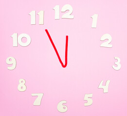 Сlock made of wooden letters arranged in a circle on a pink background. The time is eleven fifty-five. Concept of time, starting new day, starting new year.