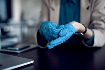 Close-up of businesswoman using protective gloves in the office due to COVID-19 pandemic.