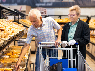 mature european couple shopping buns and bread in bakery section of supermarket