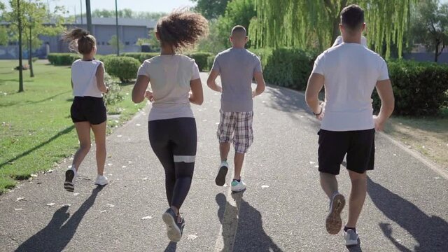 Group of unrecognizable mixed-race young friends running at the city park in the morning - View from back of people jogging in the nature - Concept of keep fit for a healthy life and live better