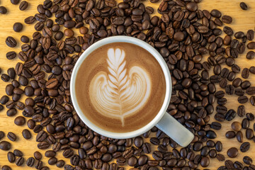Top view of a mug of coffee with beans on wooden background.