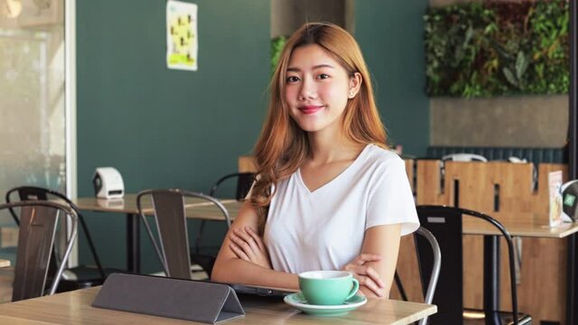 Asian young female barista standing behind counter in coffee shop. beautiful woman cafe owner in apron face looking at camera.