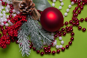 Single red New Year ball on red and white beads with a Christmas tree branch and red berries on a green background: Christmas background