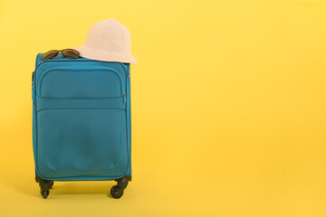 Fototapeta na wymiar Blue checked suitcase on a yellow background with a straw hat for sun protection and sunglasses: tourist concept, travel, place for text