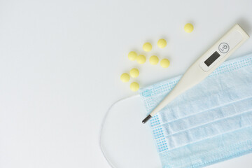 Electronic thermometer, medical mask and pills on a white background