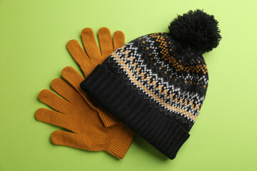 Woolen gloves and hat on green background, flat lay