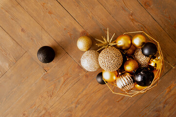gold, beige, and black glitter balloons for Christmas decorations spilled out of a metal black basket on the wooden floor. Christmas tree decoration process. selective focus