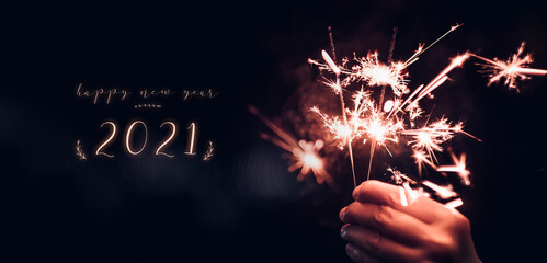happy new year 2021 text with hand holding burning Sparkler firework blast with on a black bokeh...
