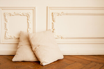two soft cozy beige pillows on wooden parquet floor and against the white stucco moulding wall. minimalism in the interior, selective focus