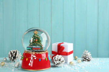 Beautiful snow globe, gift box and Christmas decor on light blue table, space for text