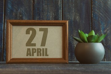 april 27th. Day 27 of month, date in frame next to succulent on wooden background spring month, day of the year concept