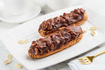 Two "snickers" eclairs with nuts and chocolate on a white plate. Traditional French dessert. Selective focus