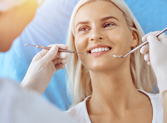 Smiling blonde woman examined by dentist at sunny dental clinic. Healthy teeth and medicine concept
