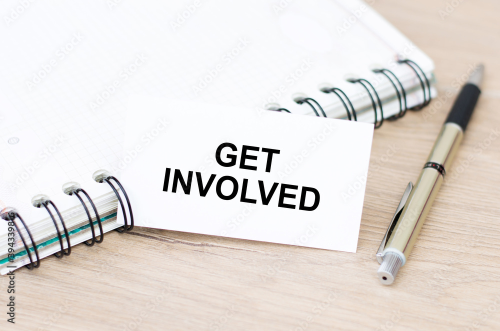 Poster business card with get involved text on the table, next to a notebook and a pen.