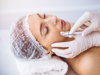 Obraz na płótnie Canvas Beautician doing beauty procedure with syringe to face of young brunette woman in sunny spa center. Cosmetic medicine and surgery, beauty injections