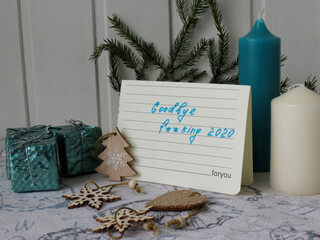 Russia, Moscow region, Lobnya, 11/21/2020: Christmas composition on a white wooden background. A note with the words "Goodbye f ** king 2020", next to the New Year's decor, candles and a sprig of spru