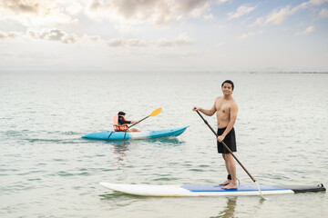 Asian man is paddling on a SUP board, standup paddler at the ocean during sunset, summer holidays vacation travel.