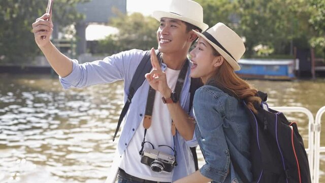 Traveler Asian couple travel in riverside Bangkok, Thailand, sweet couple taking photo  spending holiday trip in sunset. Young fun happy Asian tourist backpacker travel.