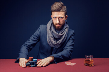 Stylish bearded Man in suit and scarf playing in dark casino, smoking cigar, drink whiskey.