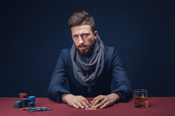 Stylish bearded Man in suit and scarf playing in dark casino, smoking cigar, drink whiskey.