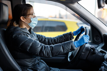 Pretty caucasian woman with glasses, anti virus medical mask and blue latex gloves driving a car with her hands on the steering wheel. Protection from the Corona COVID-19 infection. Healthcare concept