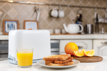 White toaster, glass of orange juice, crispy toasted bread on the plate and fresh oranges on wooden board. Looking yummy for morning meal. Kitchen interior. Fresh delicious breakfast concept.