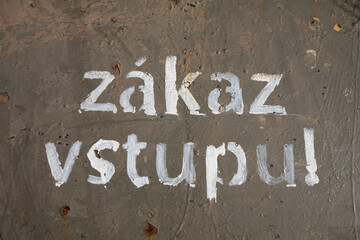 Zakaz vstupu (translation from Czech: No admittance / No entry) - handwritten text is painted by white paint on rusty and tarnished metal surface.
