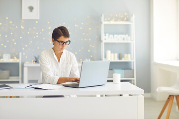 Business lady in glasses sitting at home and working on laptop online