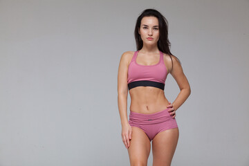 Attractive young brunette woman in pink sportswear is posing isolated on grey background